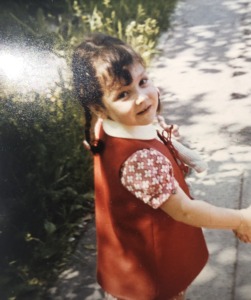 A 4 years old girld with 2 breads in a read dress looking over her shoulder