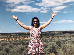 Young women standing in the desert, smiling with her arms raised ad of embracing the world