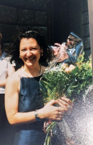 A young laughing women in a blue dress standing and holding a bouquet of flowerns in her hands