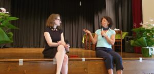 two women sitting on stage with two microphones in hand and talking to each other