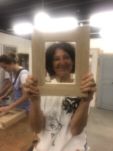 A woman with a white blouse and dark hair holding a wooden frame infront of her head