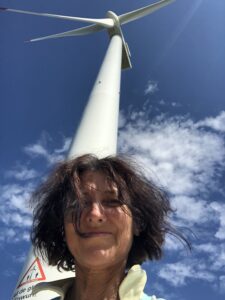 A woman with dark hair standing infront of a huge wind mill