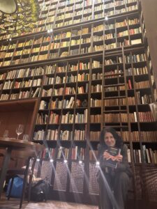 a wall with 3000 bookd and a womend sitting on a ladder infront of the books holding a book with the title "Change Your Energy - Change Your Life" in her hands